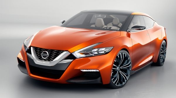Front view of the Nissan Sport Sedan shown in a shiny orange Strad Amber color, with boomerang shaped headlights, chrome grille, and 21-inch tires