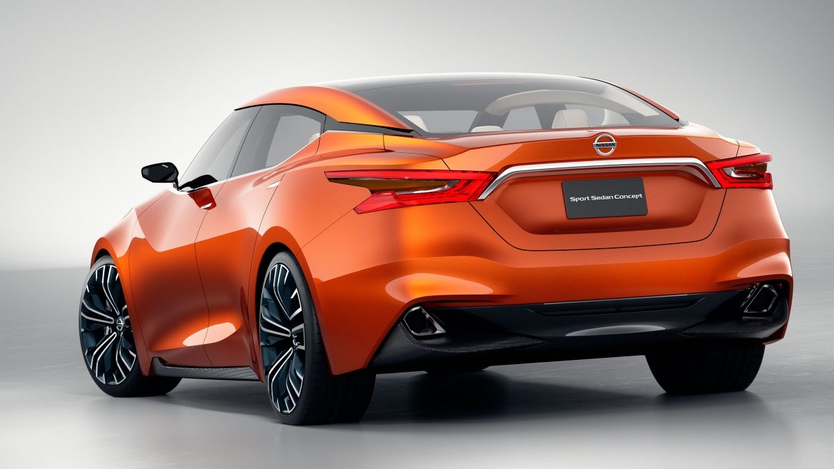 Rear side view of the Nissan Sport Sedan shown in a shiny orange Strad Amber color, with boomerang shaped taillights and 21-inch tires