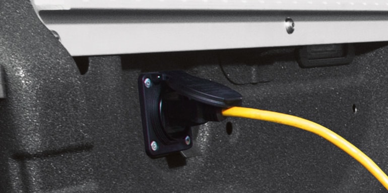 Caja de la Nissan TITAN 2024 con el cable amarillo enchufado al tomacorriente de 120 voltios 