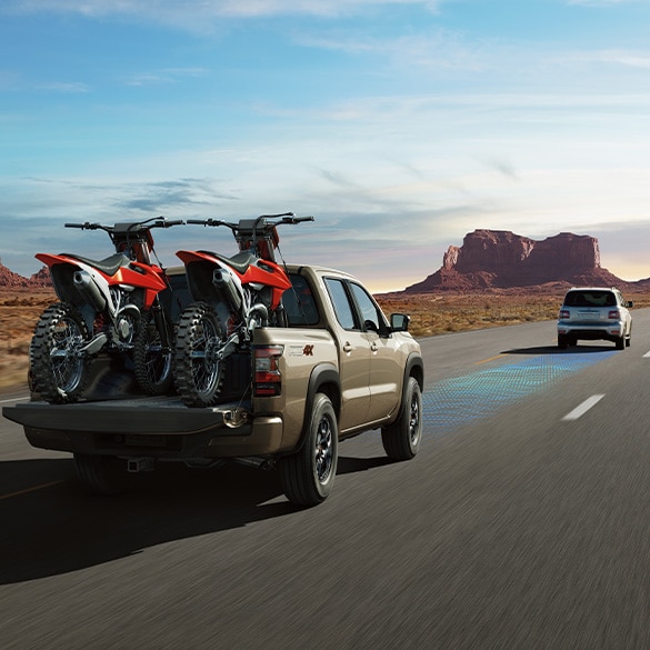 Nissan Frontier 2024 alejándose de la cámara por una carretera desierta con dos motocicletas en la caja.