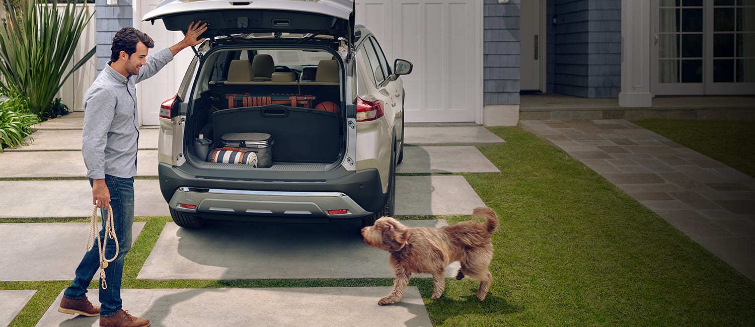 Nissan Rogue 2023 con la escotilla abierta, un hombre con una correa y un perro para ilustrar la capacidad de carga.