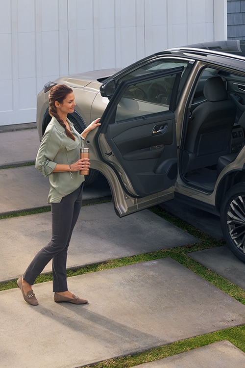 Nissan Rogue 2024 estacionado en una entrada con una mujer abriendo la puerta trasera